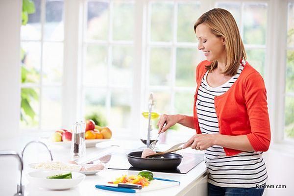 Woman Standing At Hob Preparing Meal In Kitchen